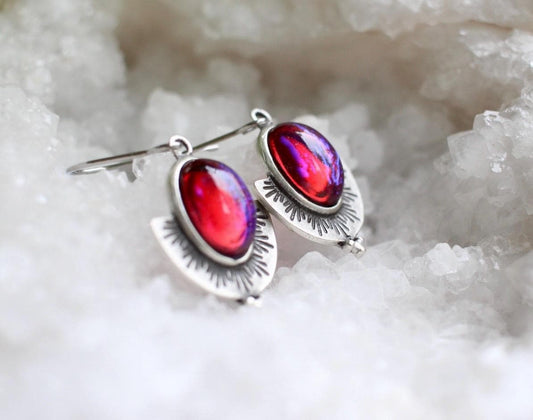 Silver earrings with red gemstones on a white crystal background