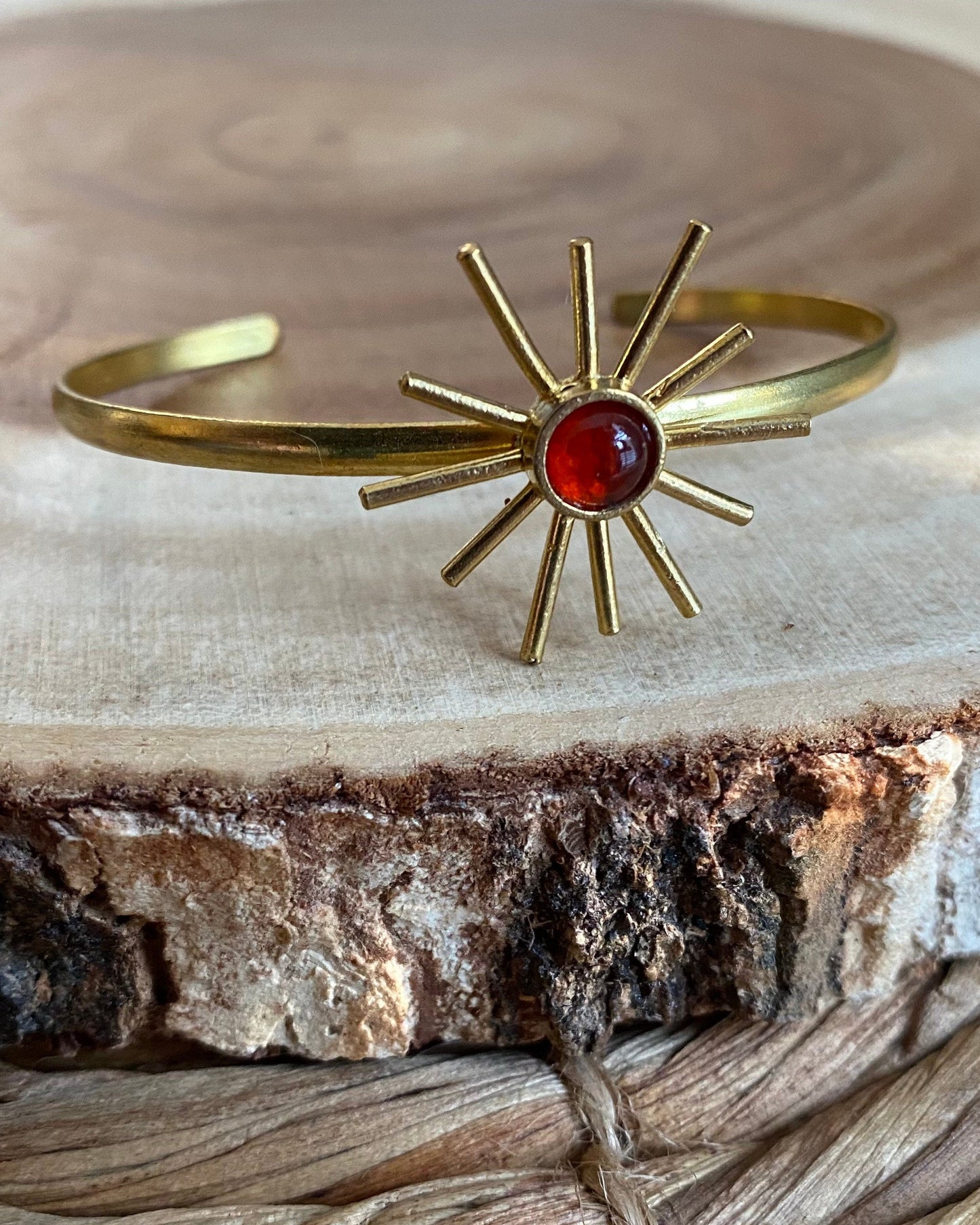Gold bracelet with a red orange gemstone on a wooden surface