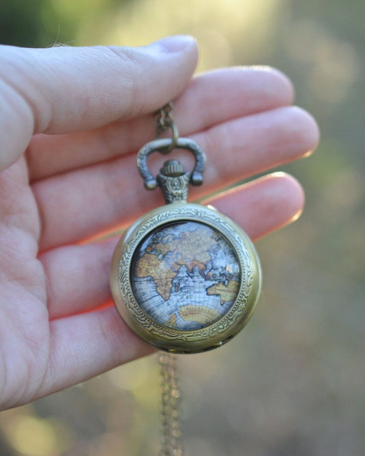 Hand holding a vintage-style pocket watch with a detailed face against a blurred natural background