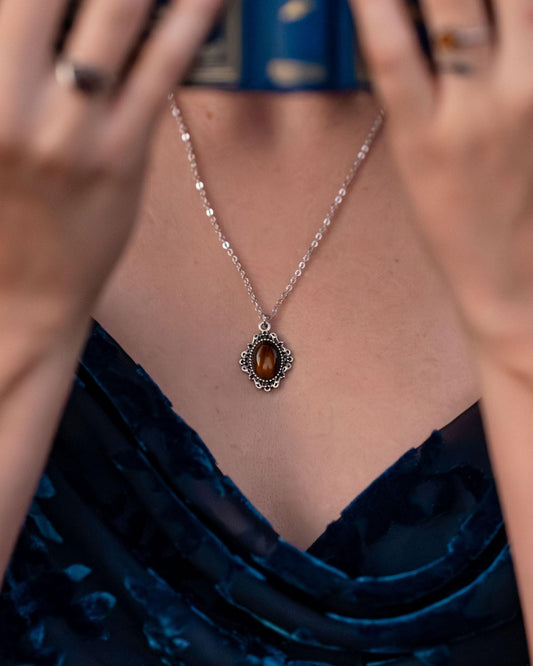 Close-up of a person wearing a necklace with a pendant, with a blurred background.