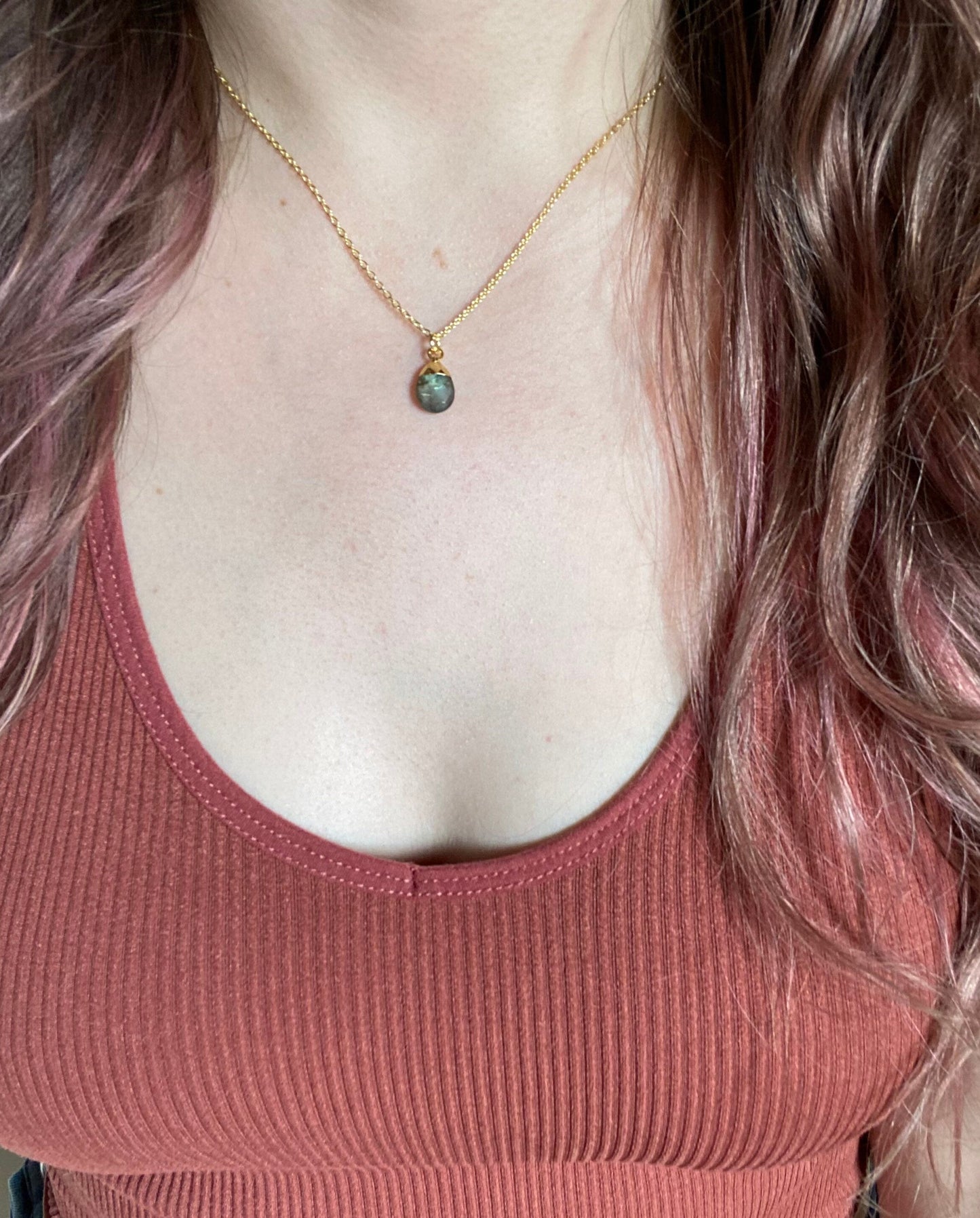 Person wearing a gold necklace with a pendant, wearing a pink tank top.