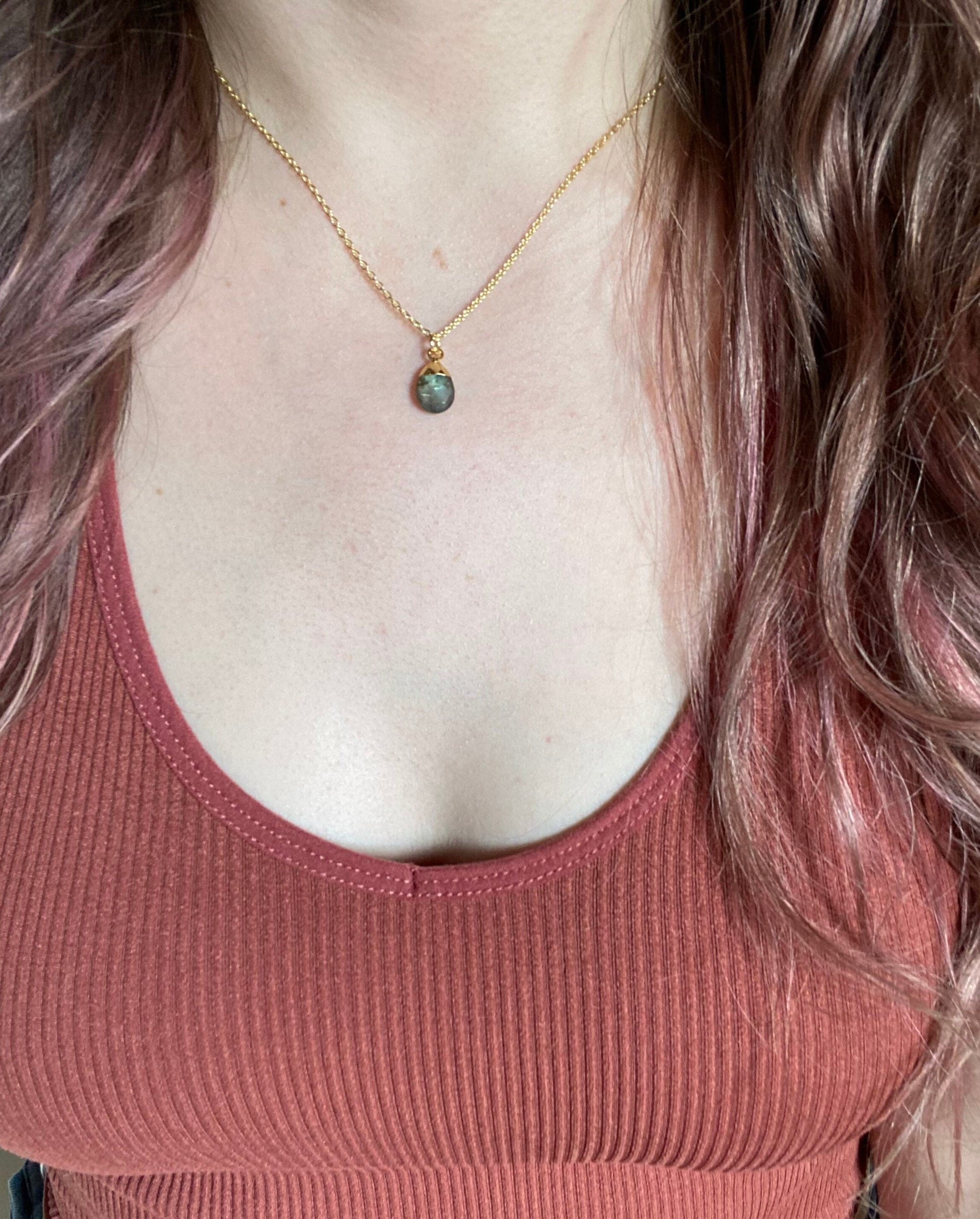 Person wearing a gold necklace with a pendant, wearing a pink tank top.
