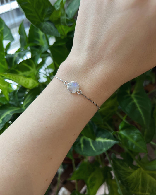 Hand wearing a silver bracelet with a gemstone against a green leafy background