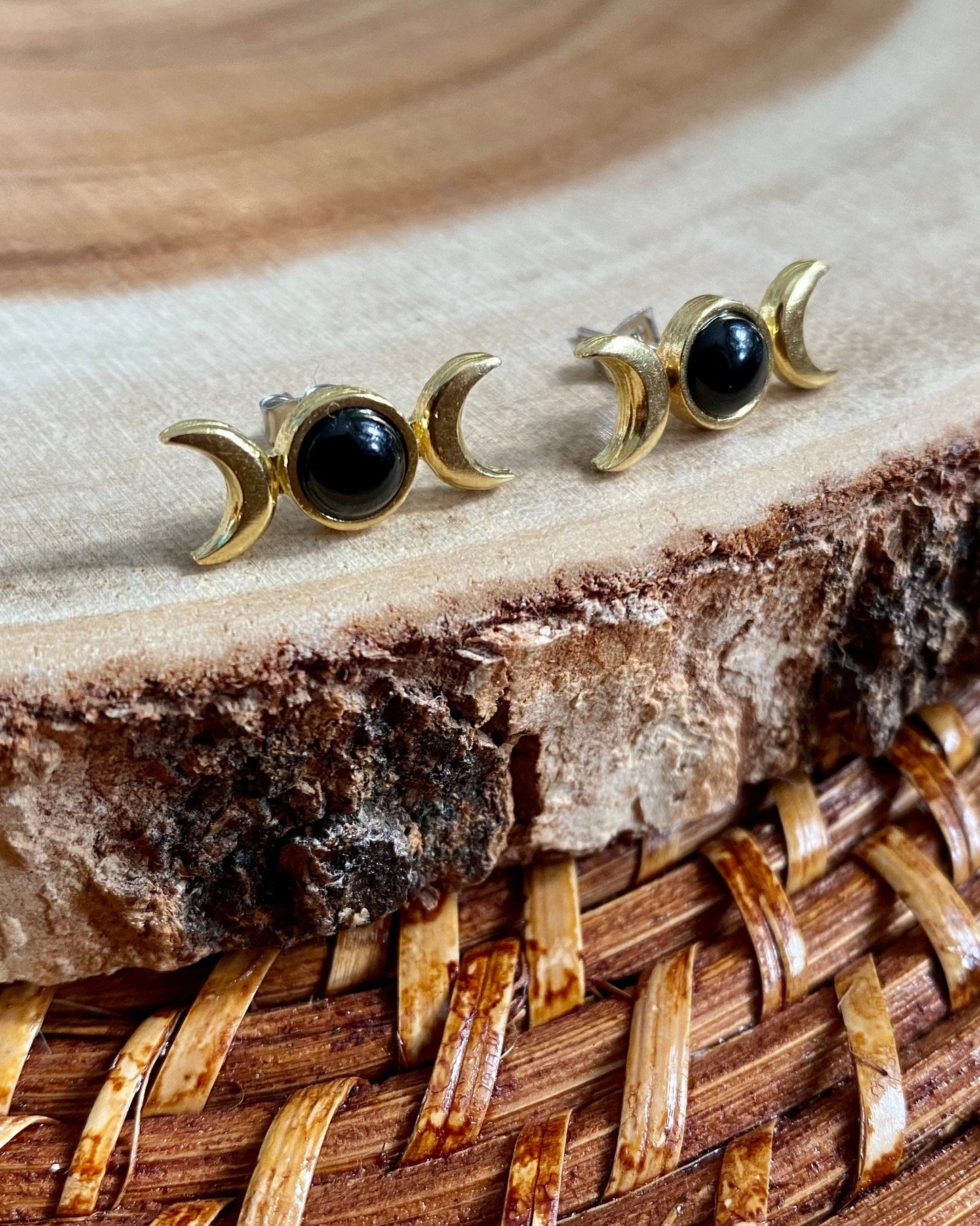 Pair of gold and black moon phase earrings on a wooden surface