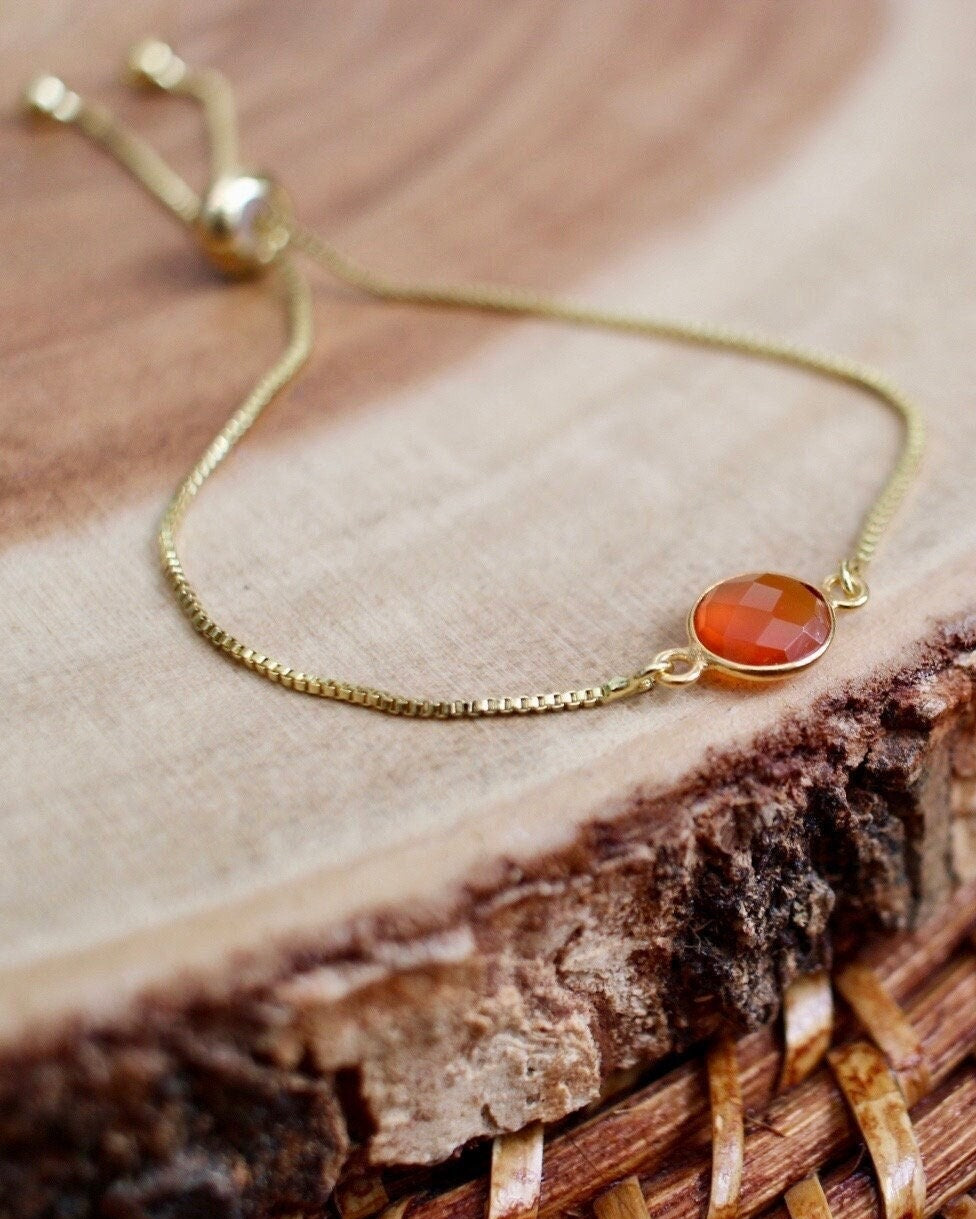 Gold bracelet with a red orange stone on a wooden surface