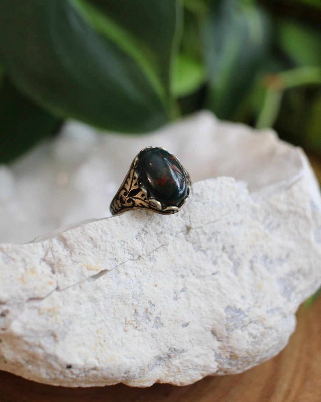Ring with a dark bloodstone sitting on a light stone surface with green foliage in the background