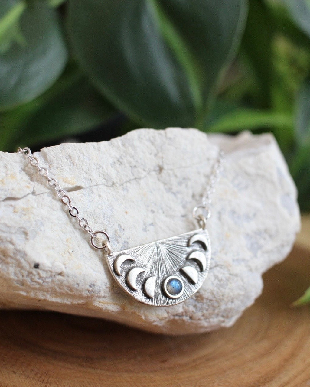 Silver necklace with a pendant on a rock with green leaves in the background