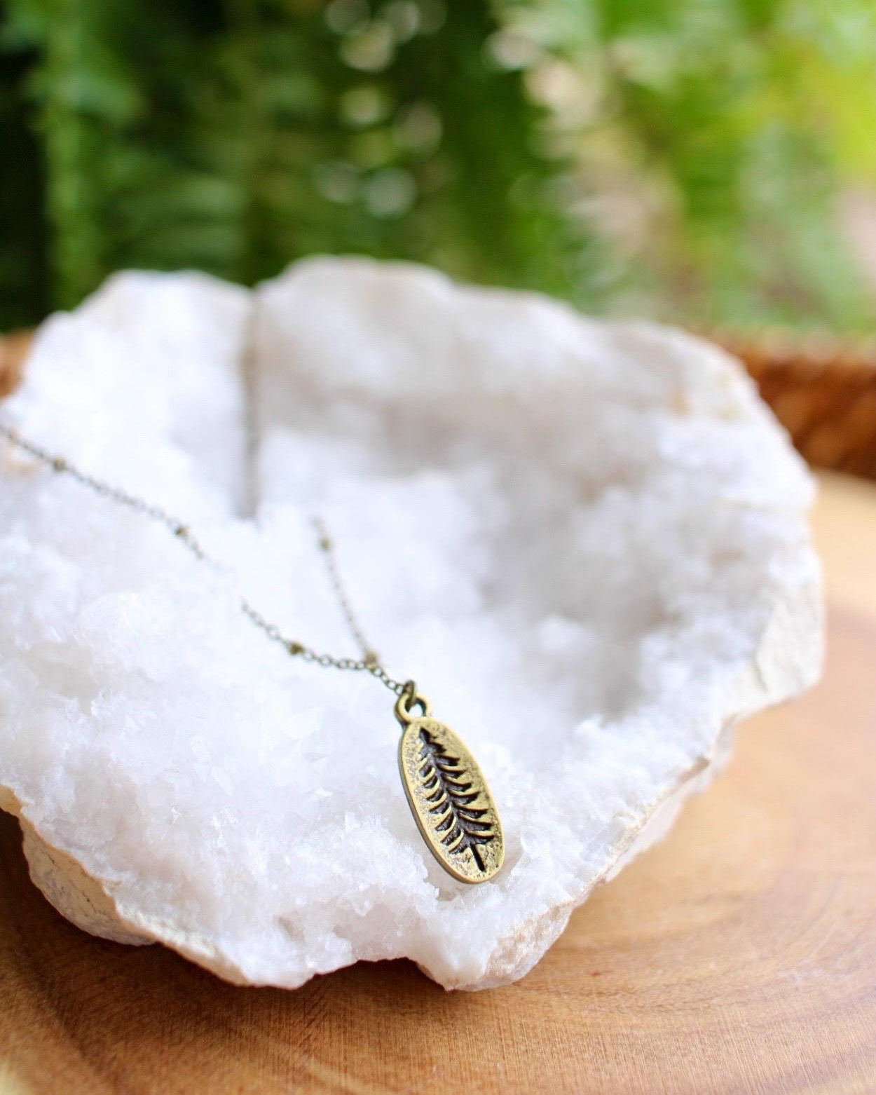 Necklace with a tree pendant on a white stone with green foliage in the background