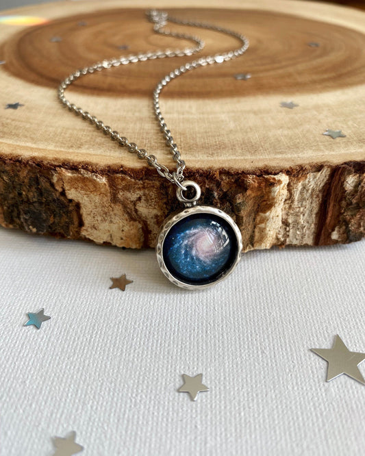 Necklace with a galaxy pendant on a wooden surface with star decorations.