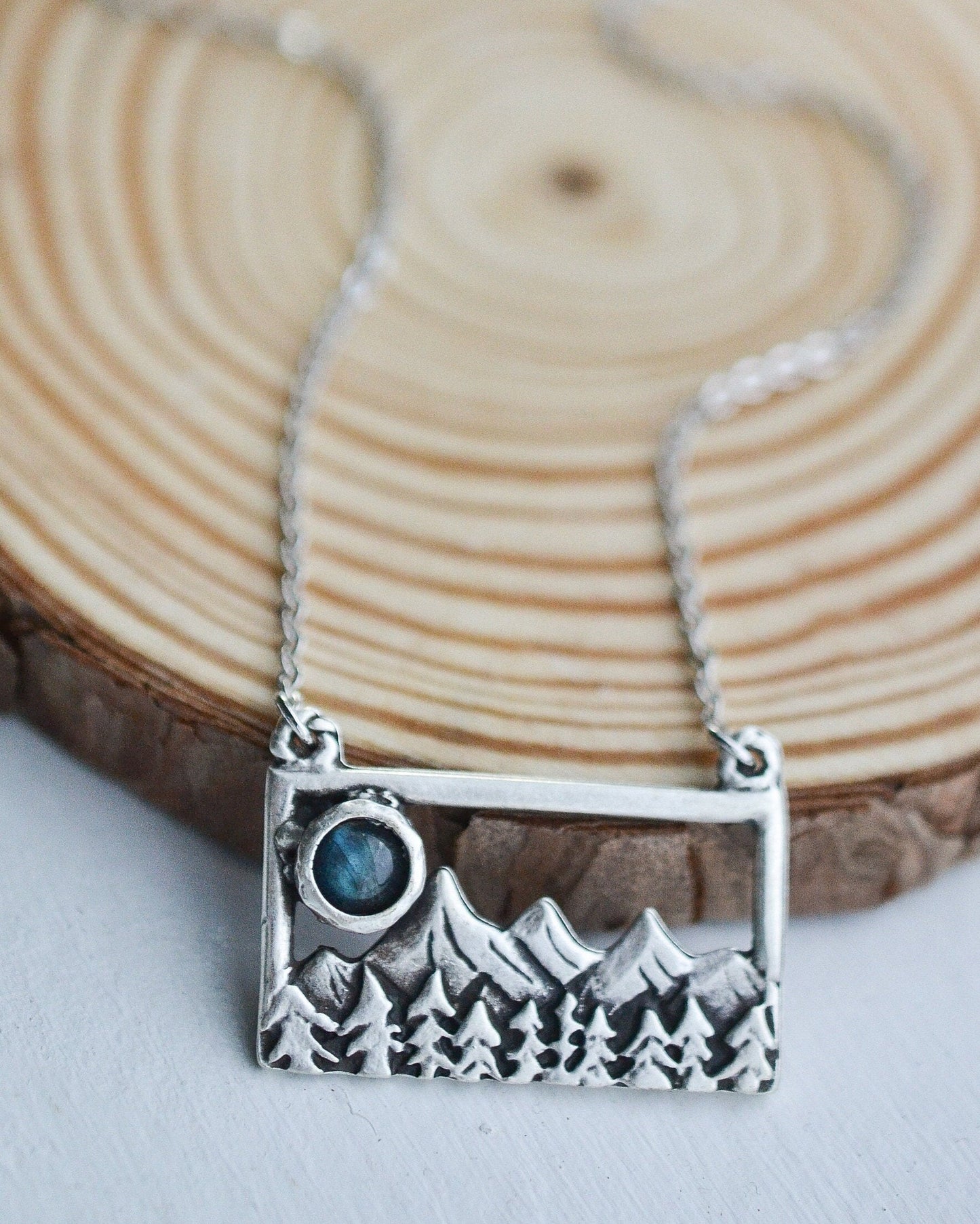Silver necklace with a mountain and moon pendant on a wooden background