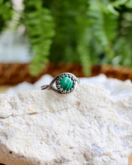 Green stone ring on top of a white crystal with greenery background