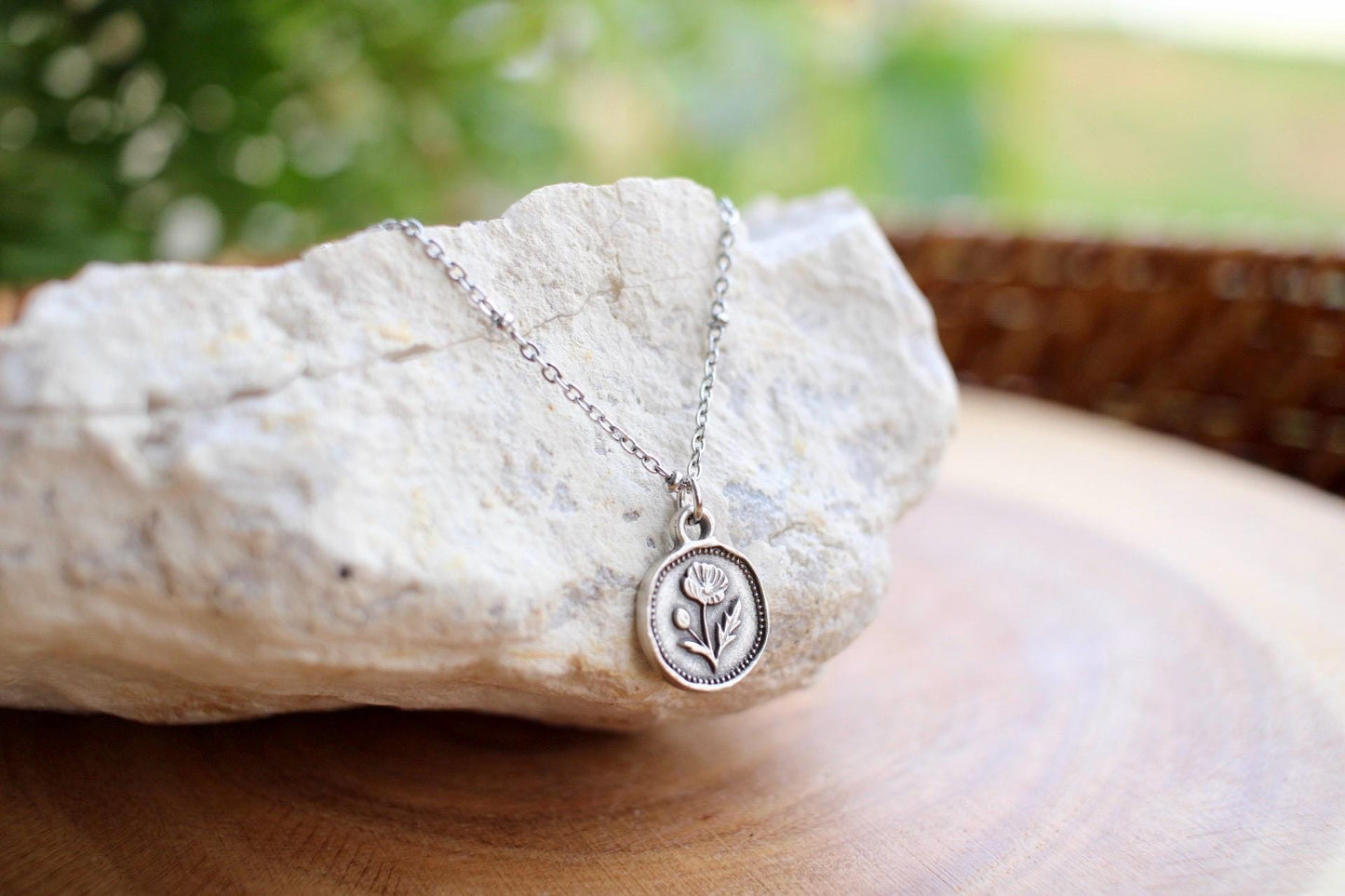 Silver necklace with a poppy flower charm on a rock with a natural background