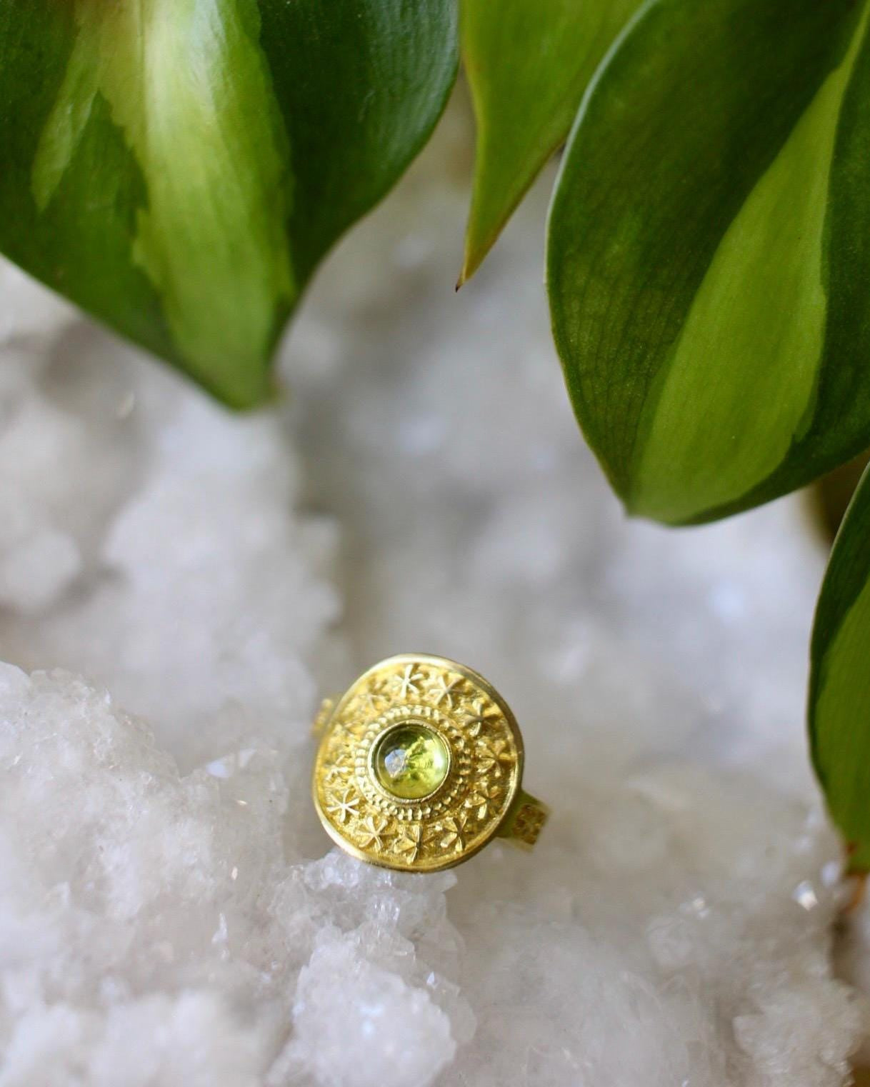 Gold ring with a green gemstone on a white stone surface with green leaves in the background