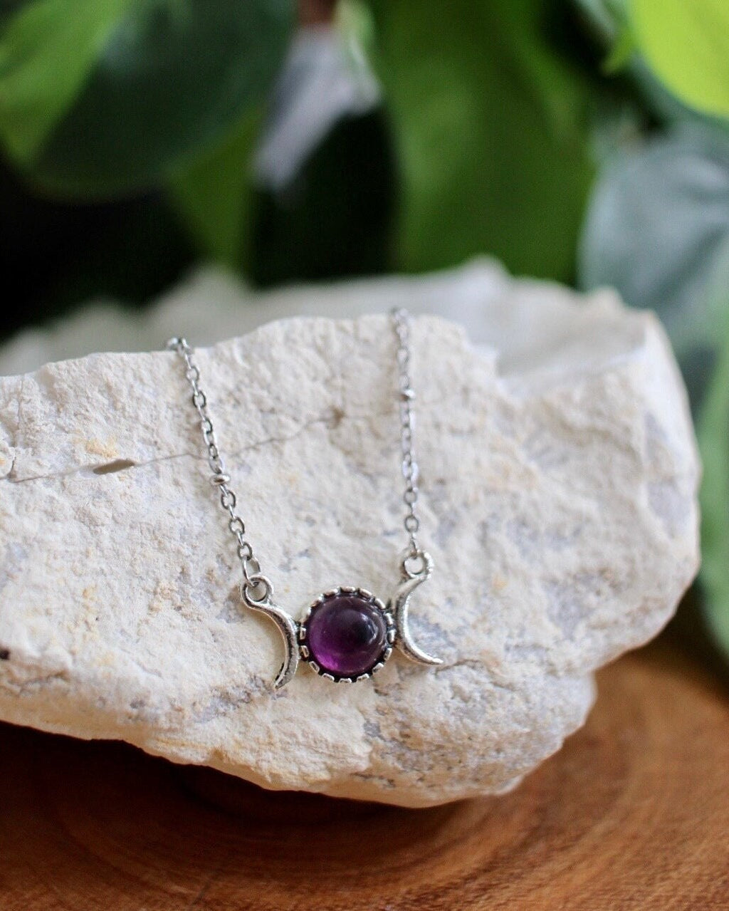 Necklace with a purple gemstone pendant on a white stone with green leaves in the background