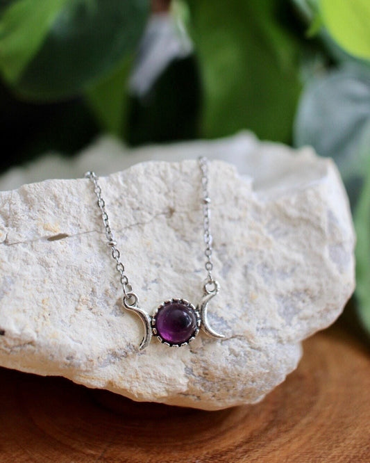 Necklace with a purple gemstone pendant on a white stone with green leaves in the background