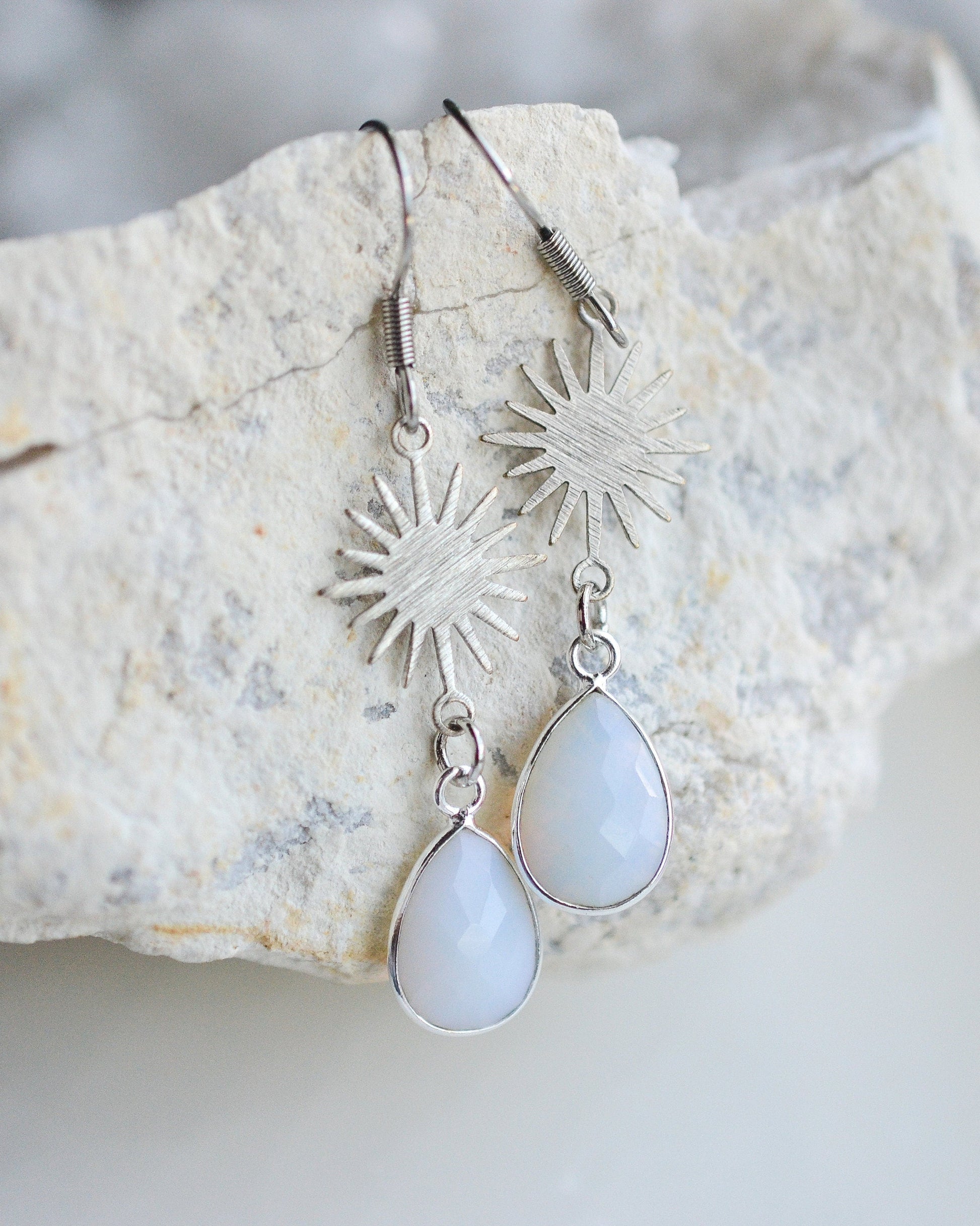 Silver earrings with teardrop-shaped white stones on a textured stone surface