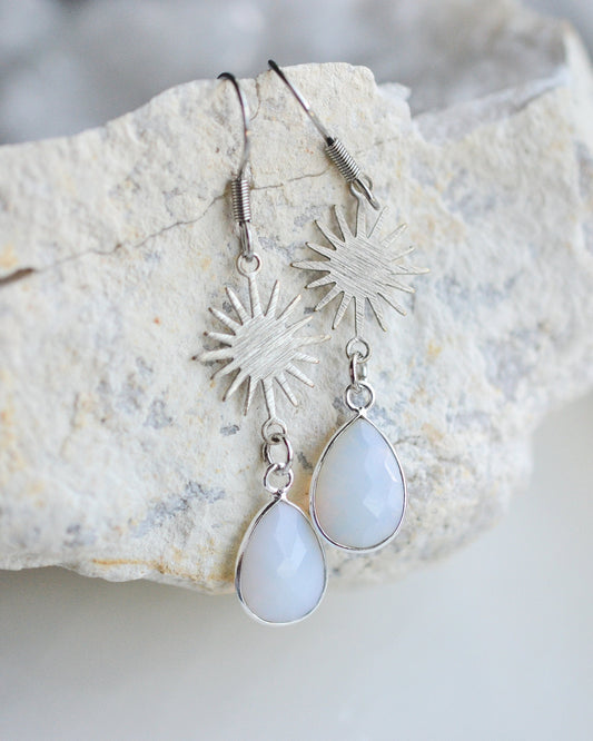 Silver earrings with teardrop-shaped white stones on a textured stone surface