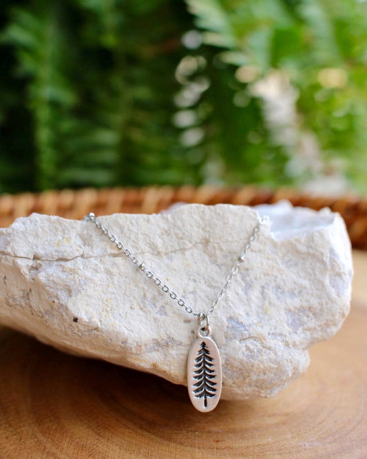 Silver necklace with a tree pendant on a rock with a fern background