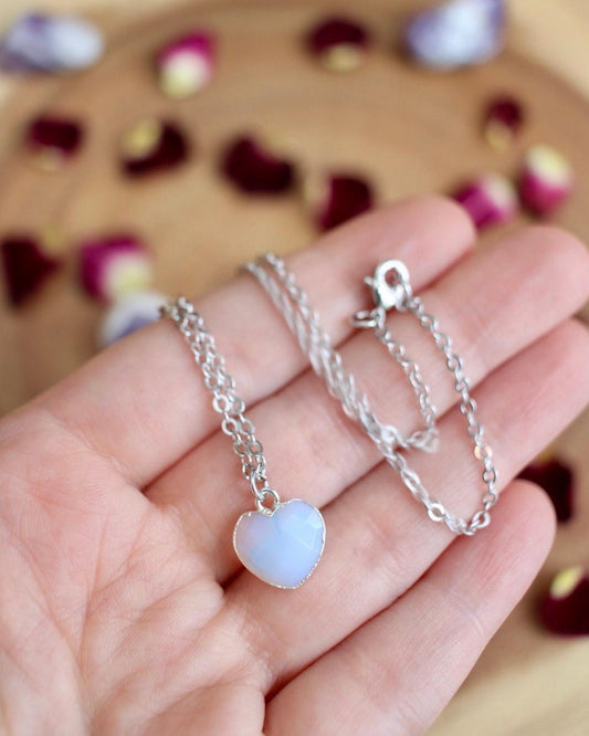 Silver necklace with a heart-shaped pendant held in a hand against a blurred background.