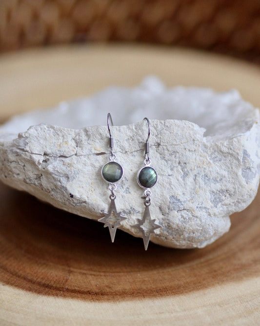 Pair of earrings with green gemstones on a white stone surface.