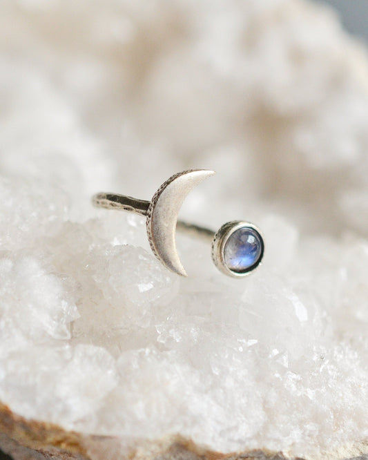 Silver ring with a moon design and gemstone on a white stone surface