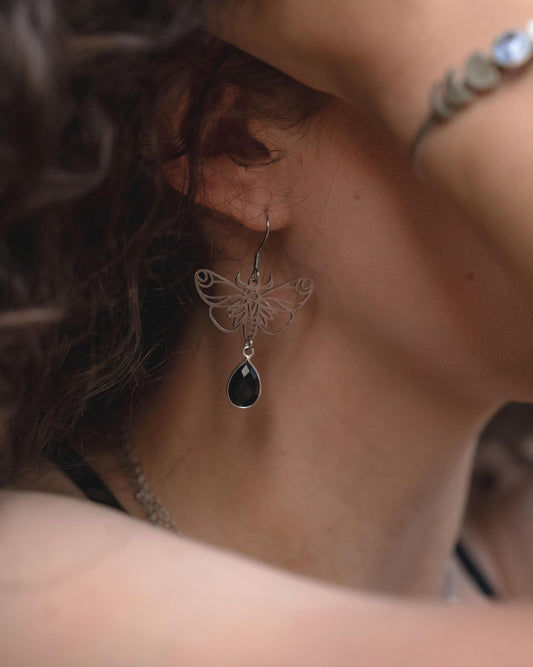 Moth earrings with black stone hanging from a woman's ear.