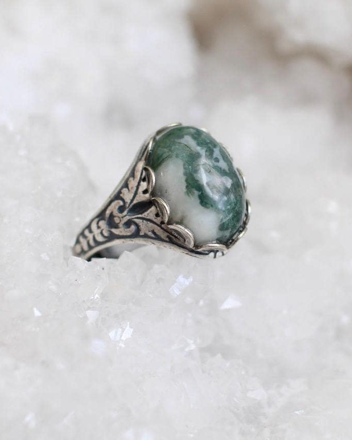 Silver ring with a green stone on a white crystal background