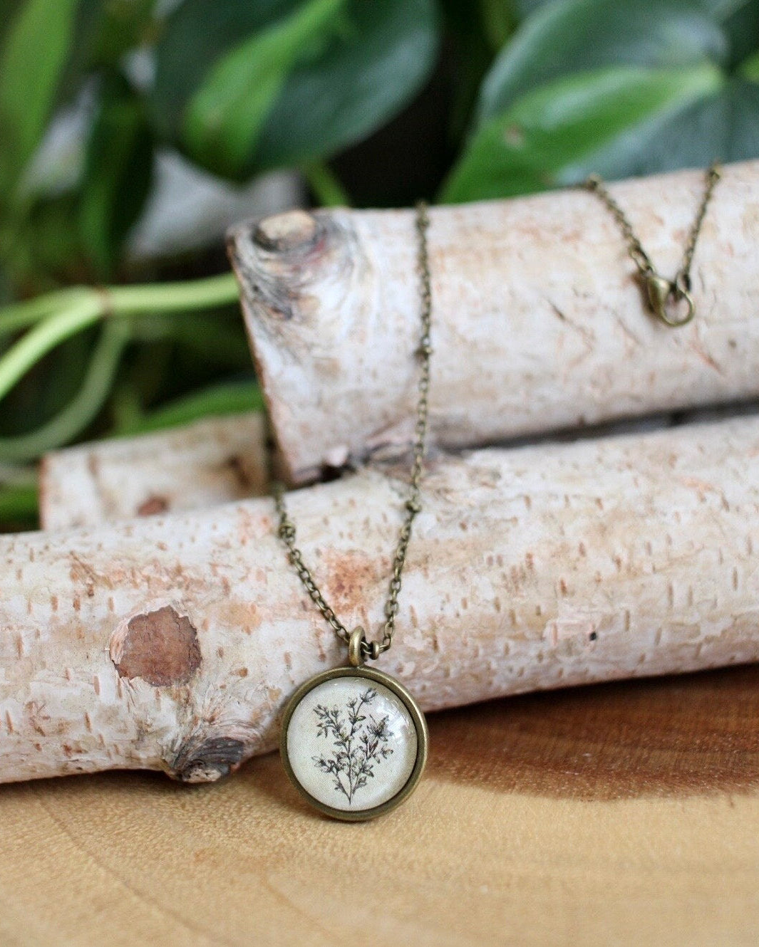 Necklace with a pendant featuring a floral design, placed on a wooden surface with greenery in the background.