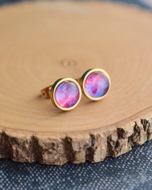 Pink and gold galaxy earrings on a wooden surface