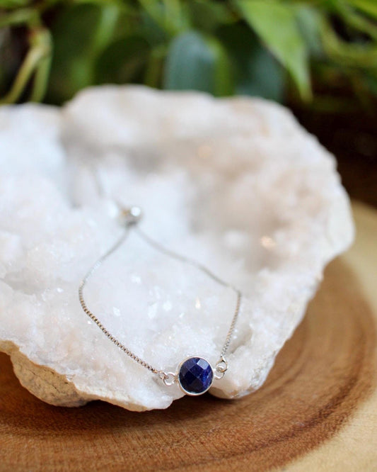 Silver bracelet with a blue gemstone on a white stone with greenery in the background