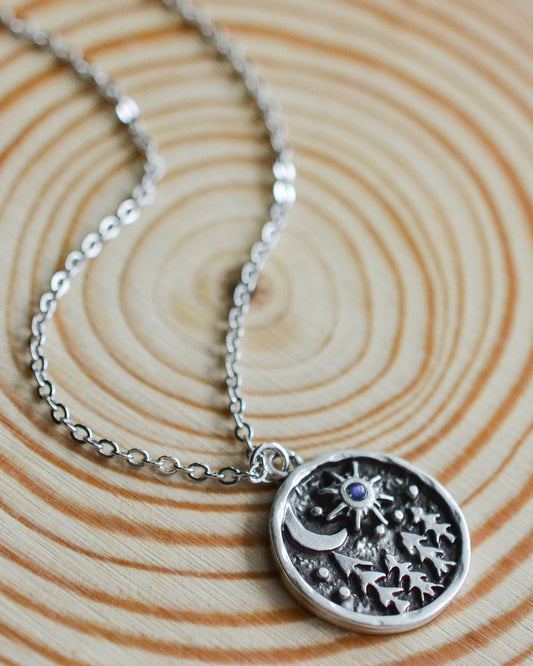Silver necklace with a celestial and pine tree pendant on a wooden surface