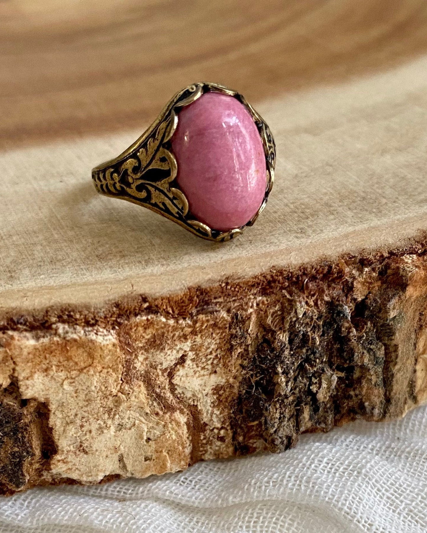 Ring with a pink stone and bronze band on a wooden surface