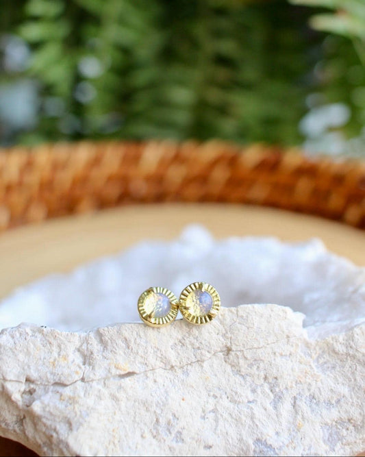 Brass stud earrings with opalite stones sitting on a white geode with a fern in the background