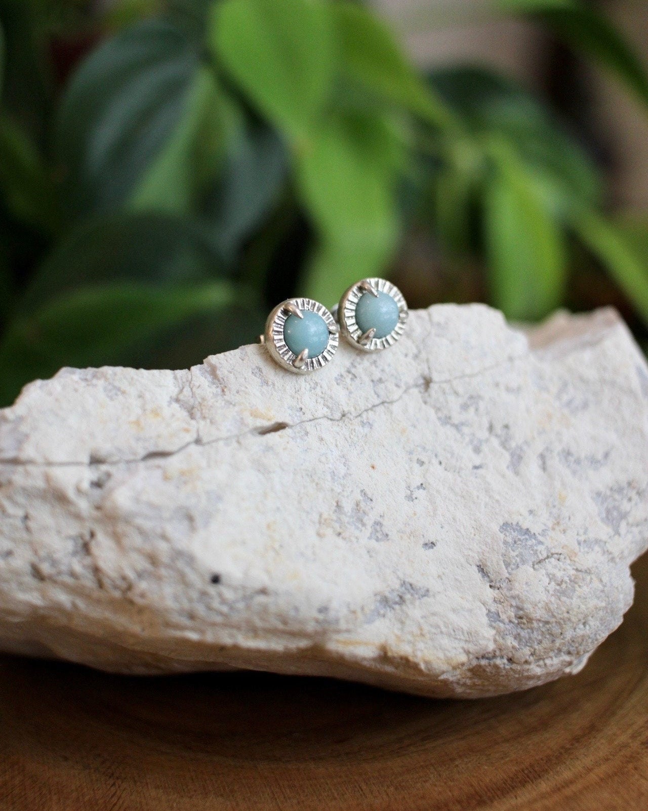 Turquoise color stone stud earrings sitting on a white crystal with a plant in the background