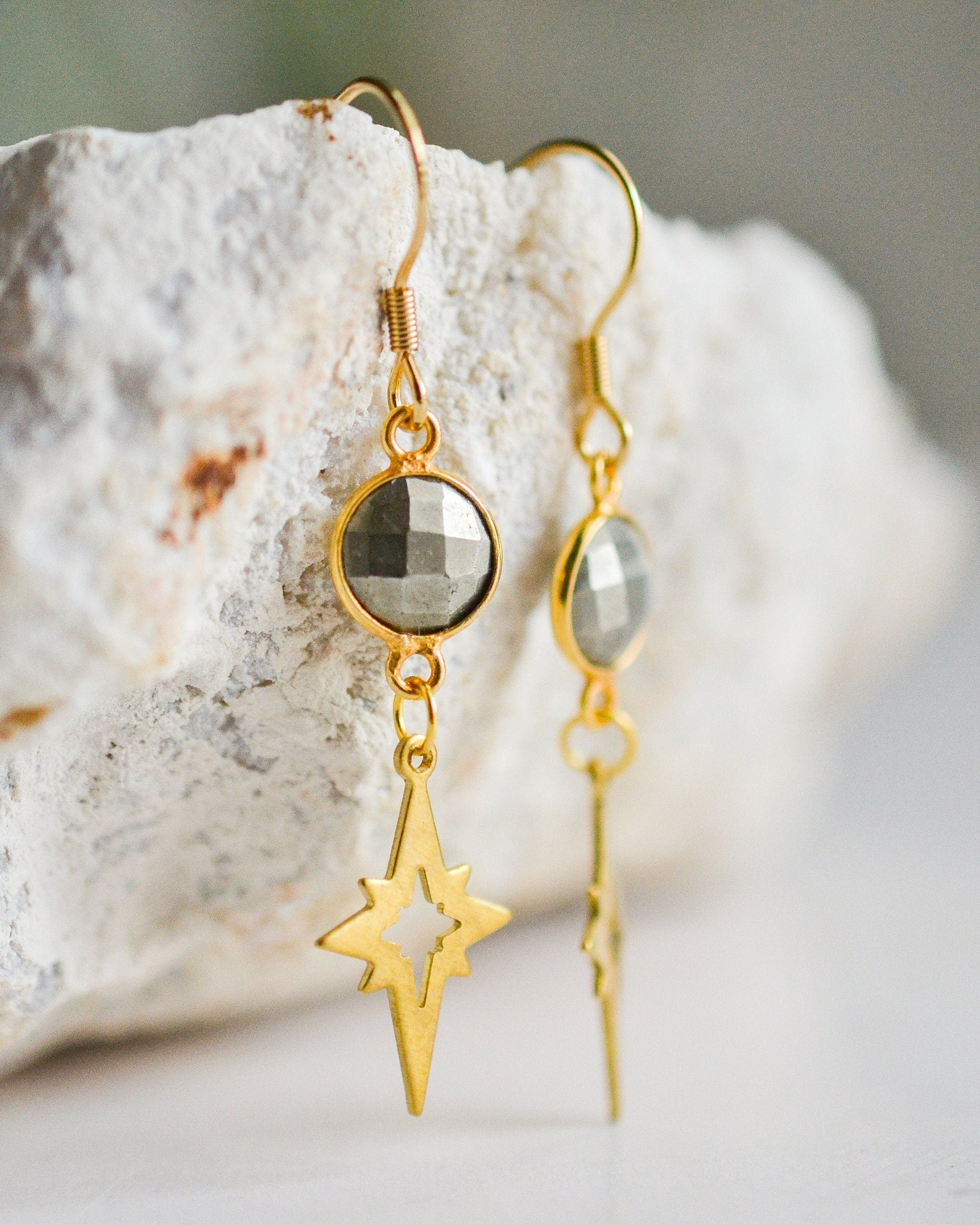 Gold earrings with star and round pendant on a stone surface