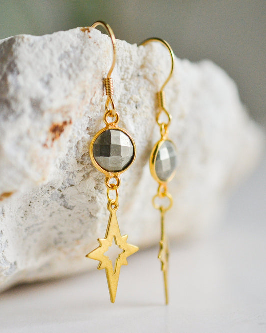 Gold earrings with star and round pendant on a stone surface