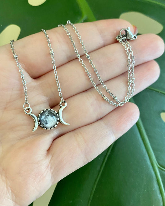 Silver necklace with a pendant held in a hand against a green leafy background