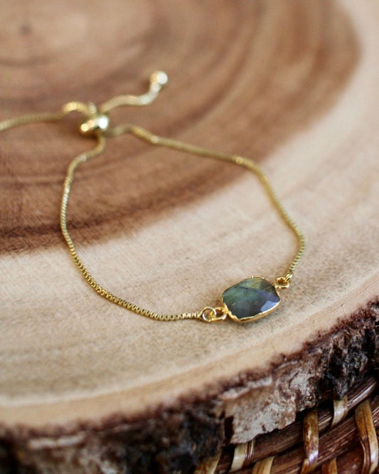 Gold bracelet with a green gemstone on a wooden surface