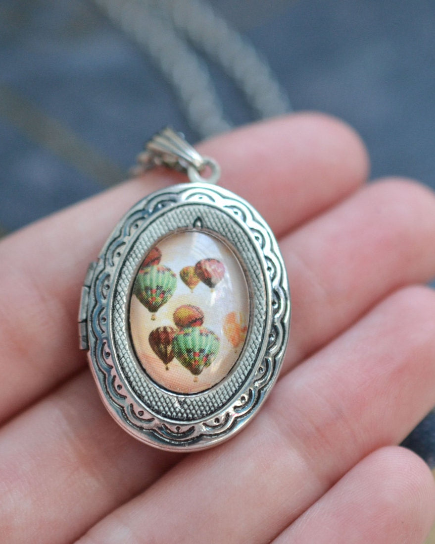 Silver locket with a decorative design held in a hand against a blurred background
