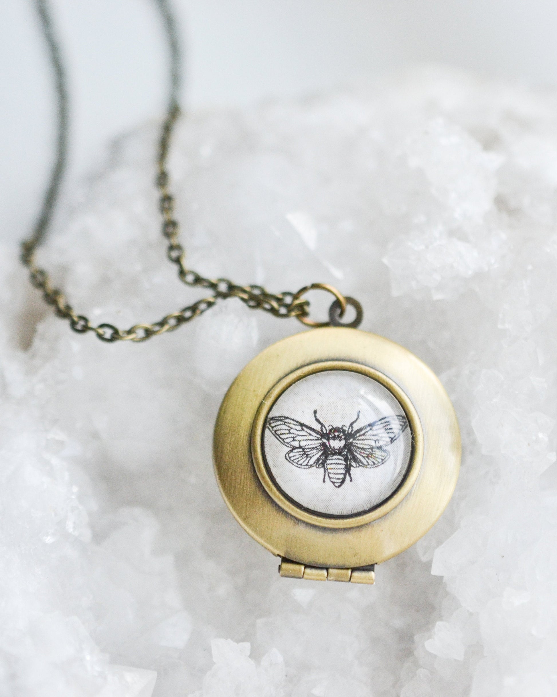 Brass locket with bee design on a white stone surface