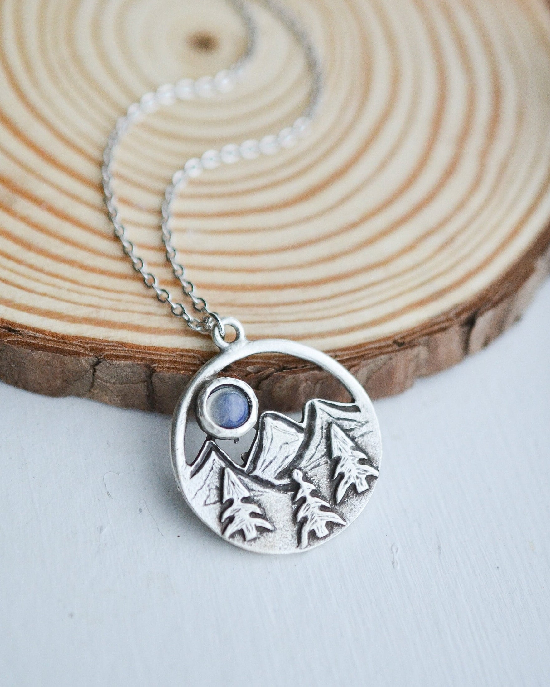 Silver necklace with a circular pendant featuring mountain designs on a wooden surface.