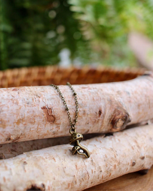 Brass mushroom necklace on a stack of birch logs with a blurred green background