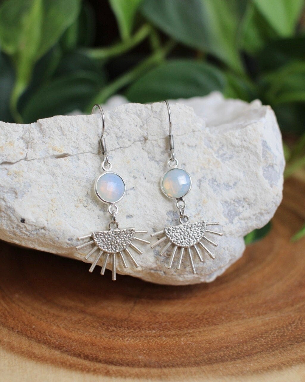 Silver earrings with gemstones on a stone surface with green leaves in the background