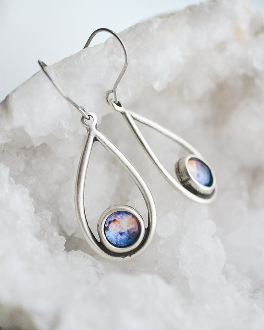 Galaxy print drop earrings laying on a white geode