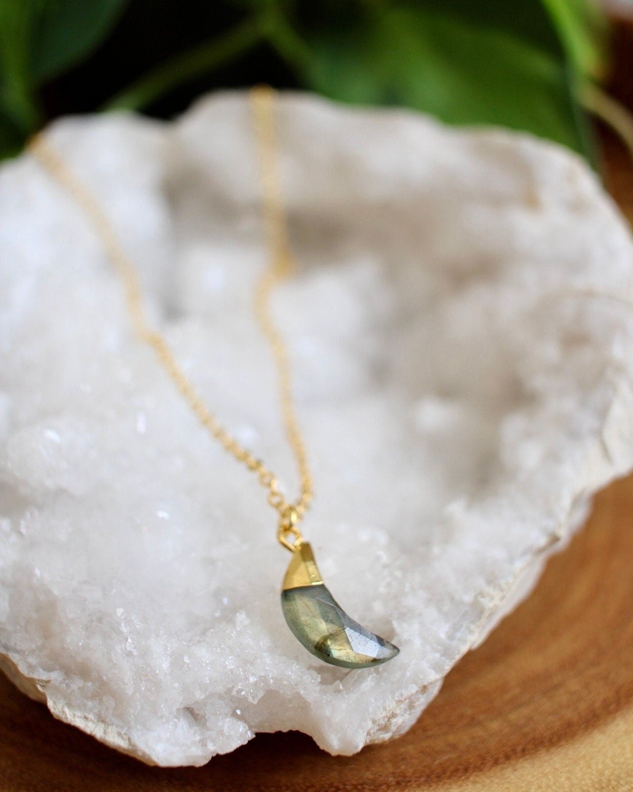 Gold necklace with a green stone moon pendant on a white stone with green leaves in the background