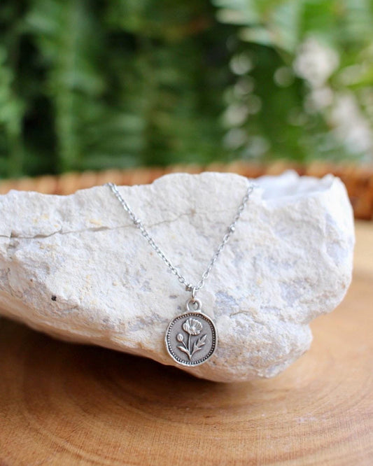 Silver necklace with a flower pendant on a rock with a natural background
