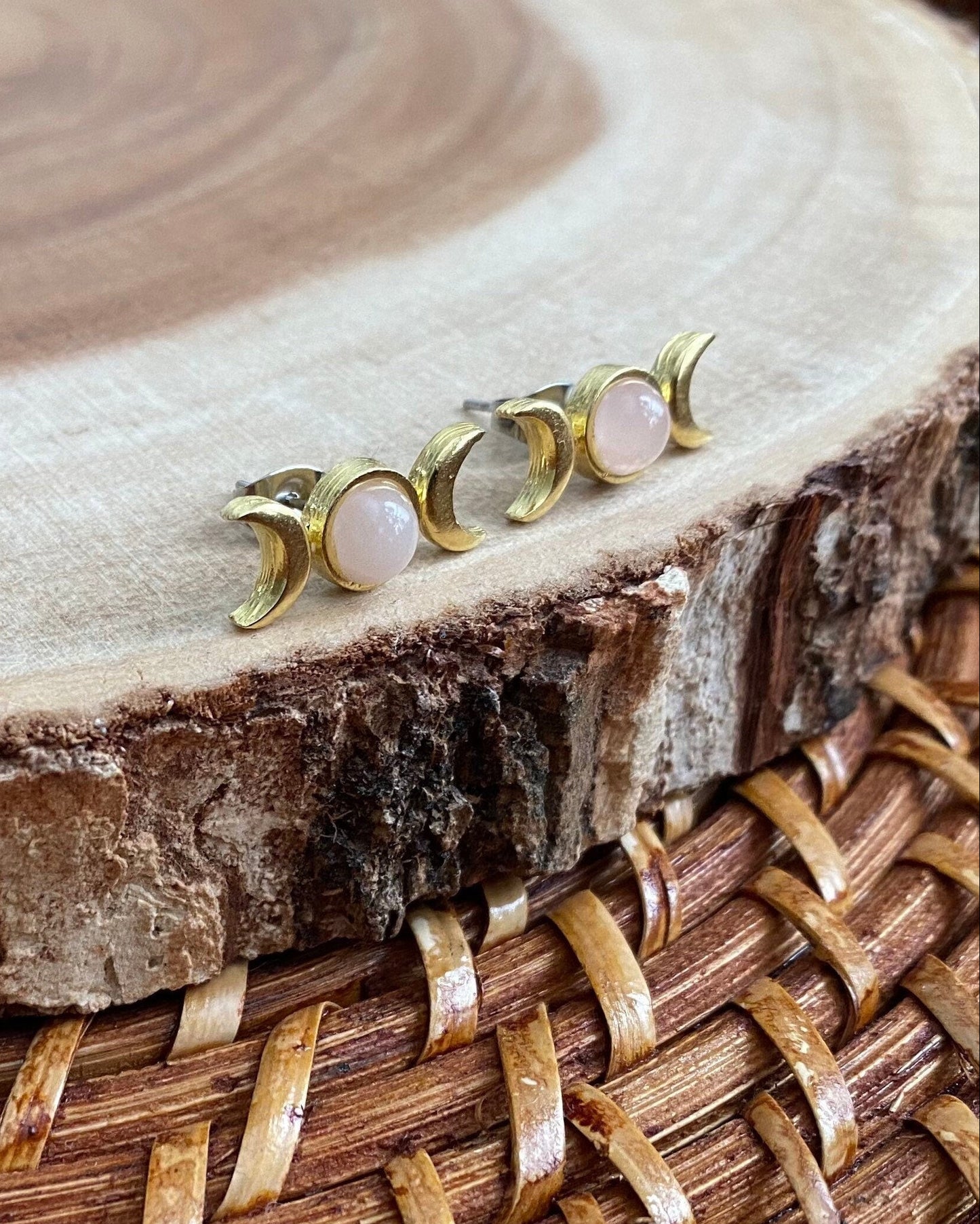 Pair of gold and pink moon-shaped earrings on a wooden surface