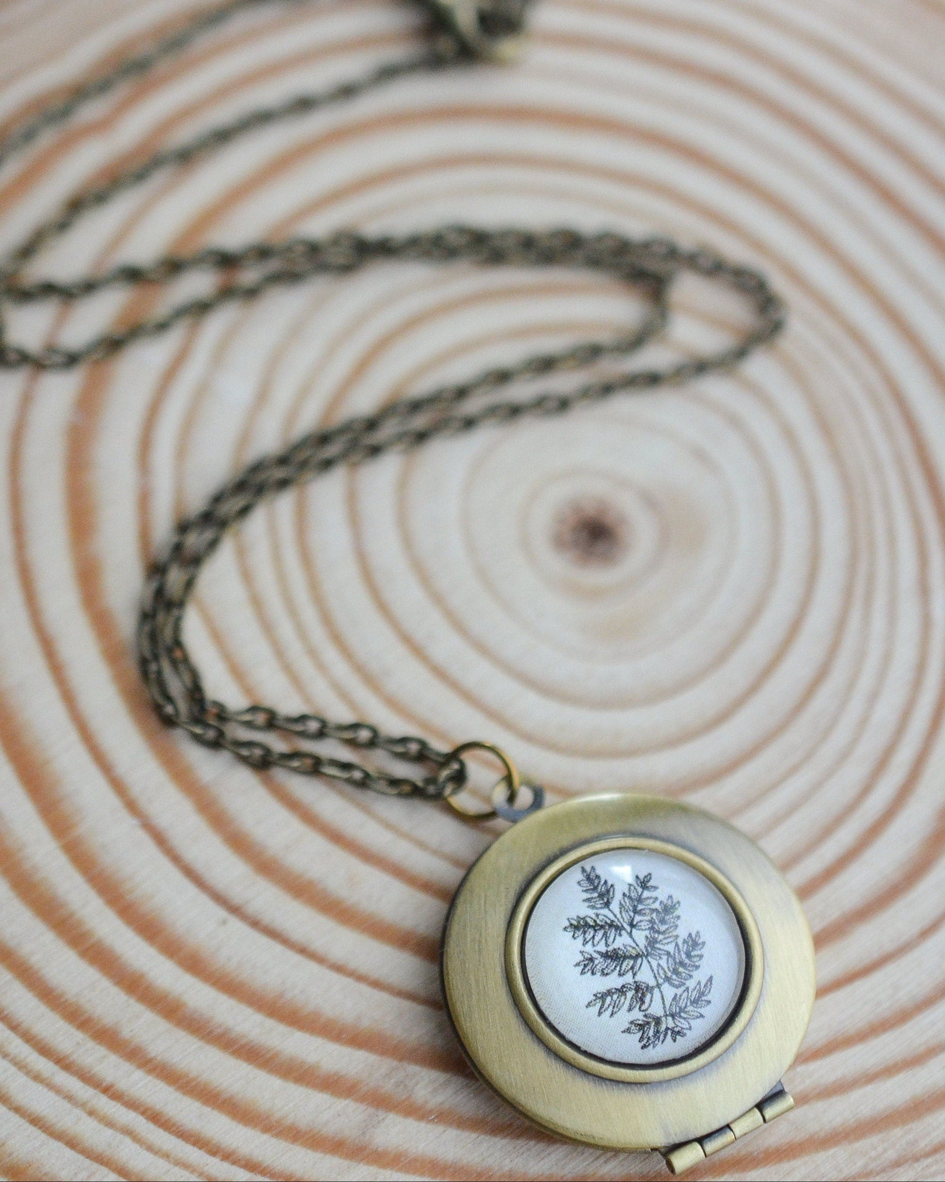Brass locket with botanical fern design on a wooden surface