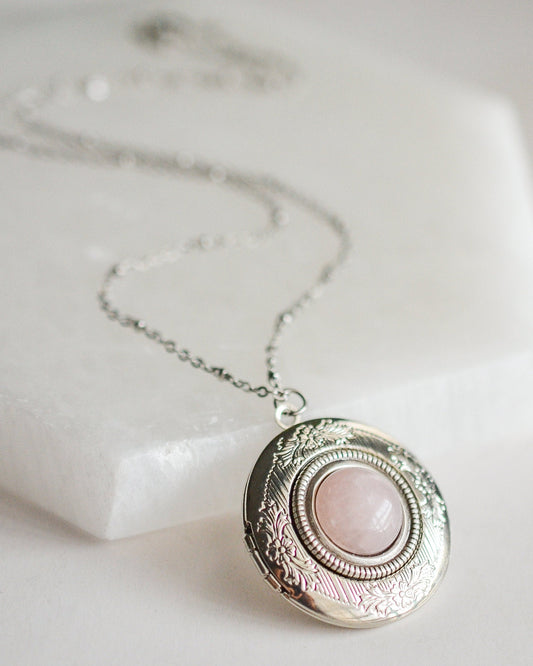 Necklace with a round locket featuring a pink stone on a light background