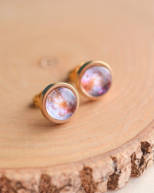 Pair of earrings with galaxy design on a wooden surface